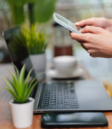 Person uses phone near laptop on table.