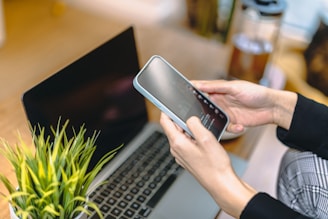 Hands hold a phone near a laptop.