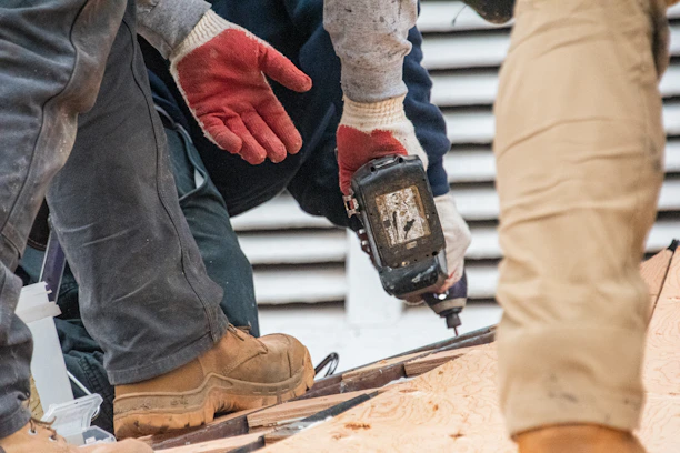 Workers are using a drill on a roof.