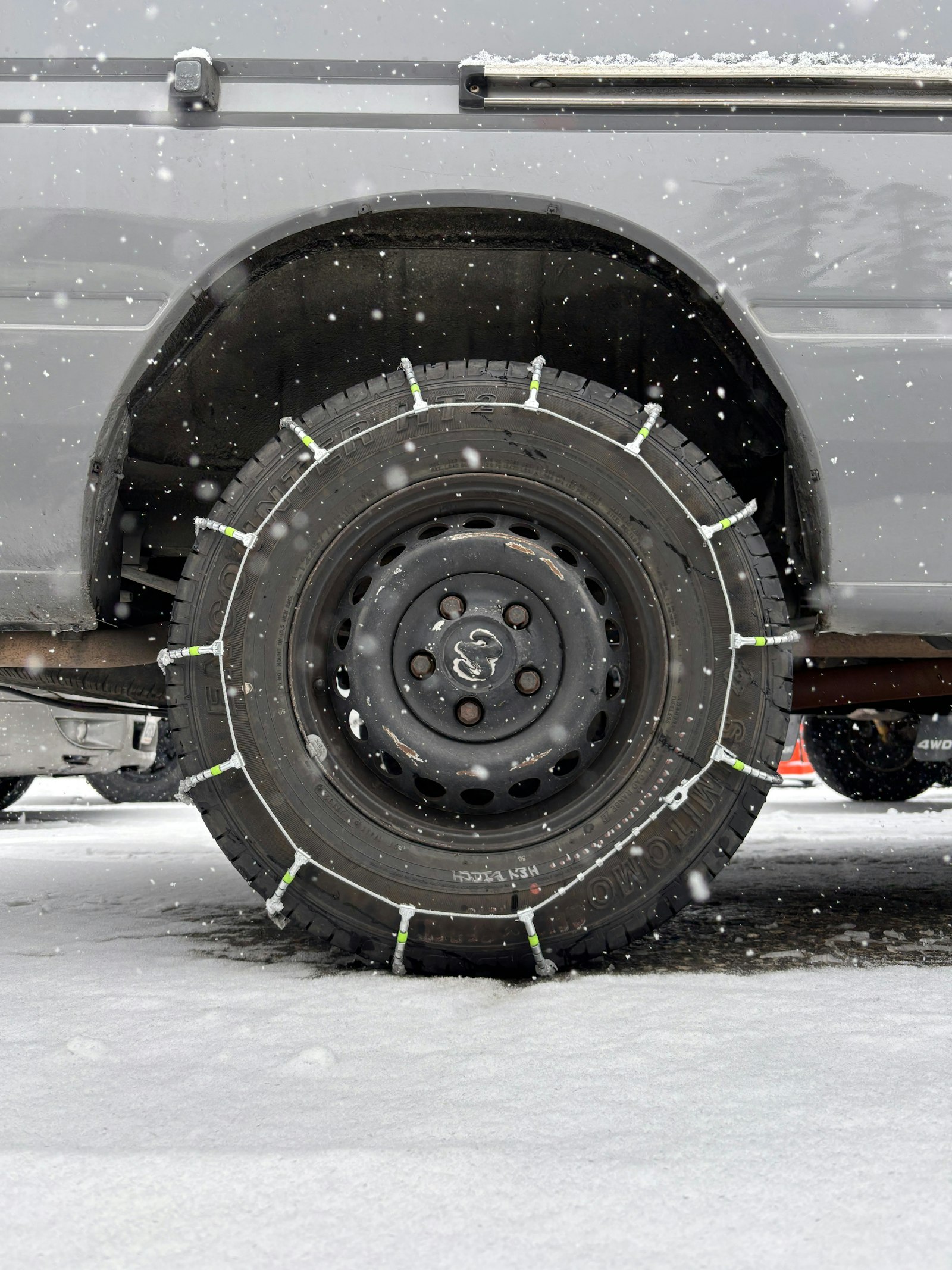 Metal snow chains fitted over a car tire on a snow-covered road