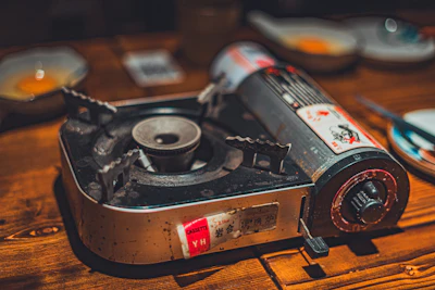 A portable gas stove sits on a wooden table.