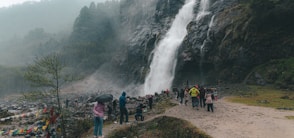 People are gathered near a large, misty waterfall.
