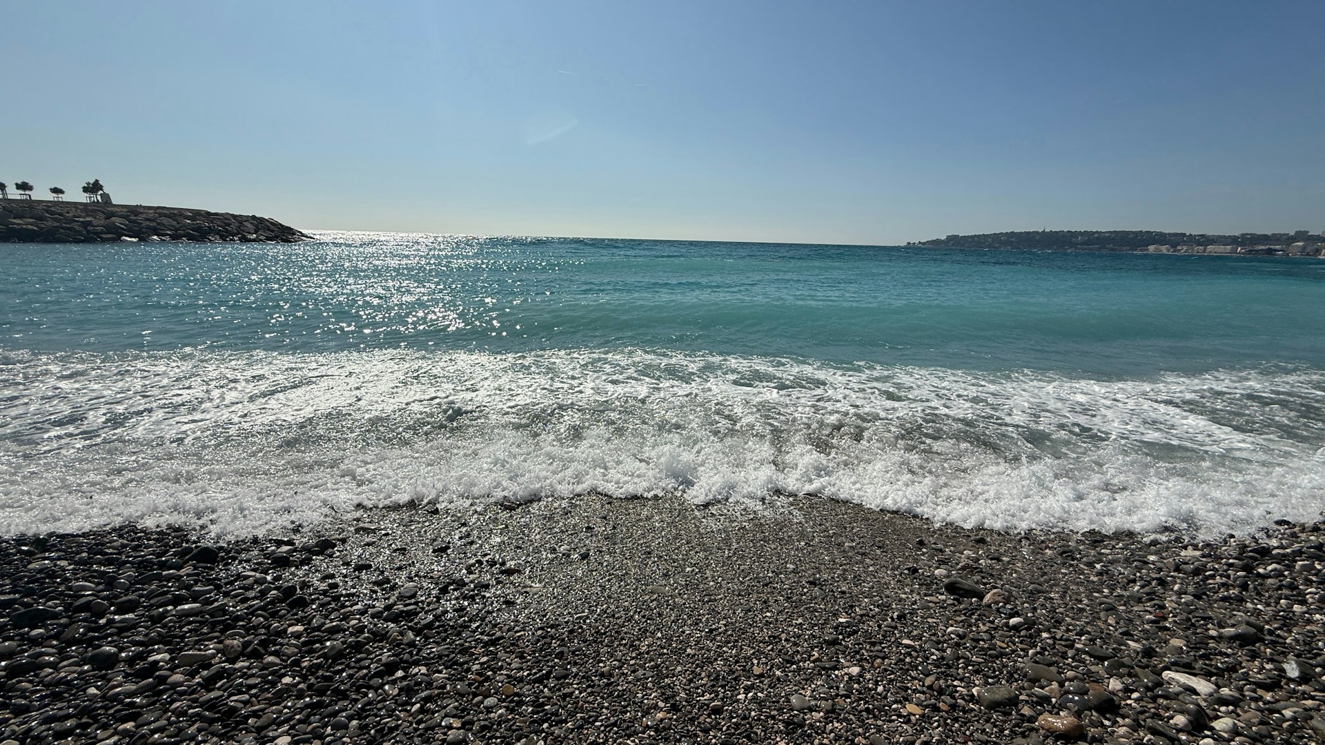 The ocean meets the shore under a bright, sunny sky.