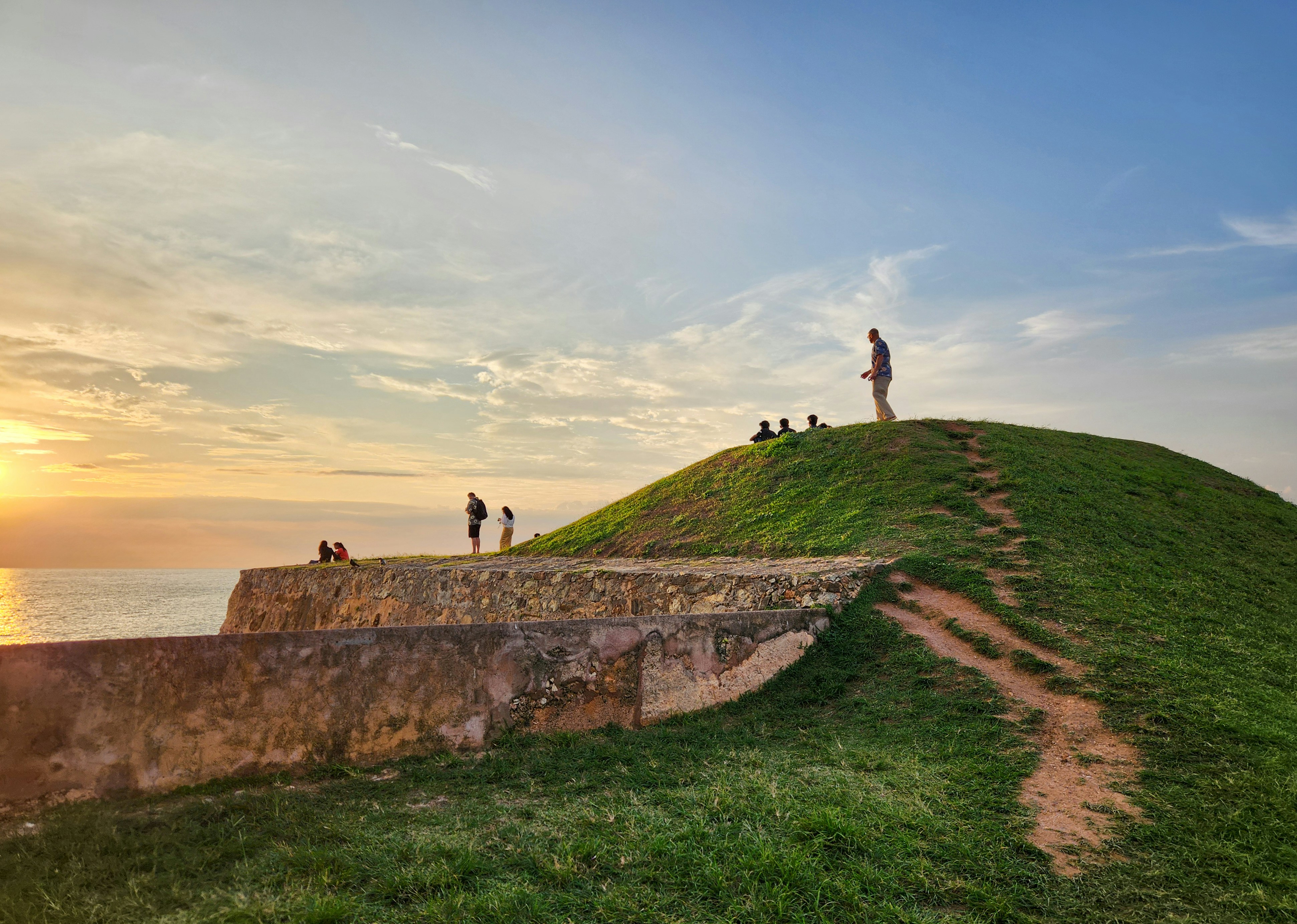 People enjoy the sunset on a grassy hill.