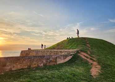 People enjoy the sunset on a grassy hill.