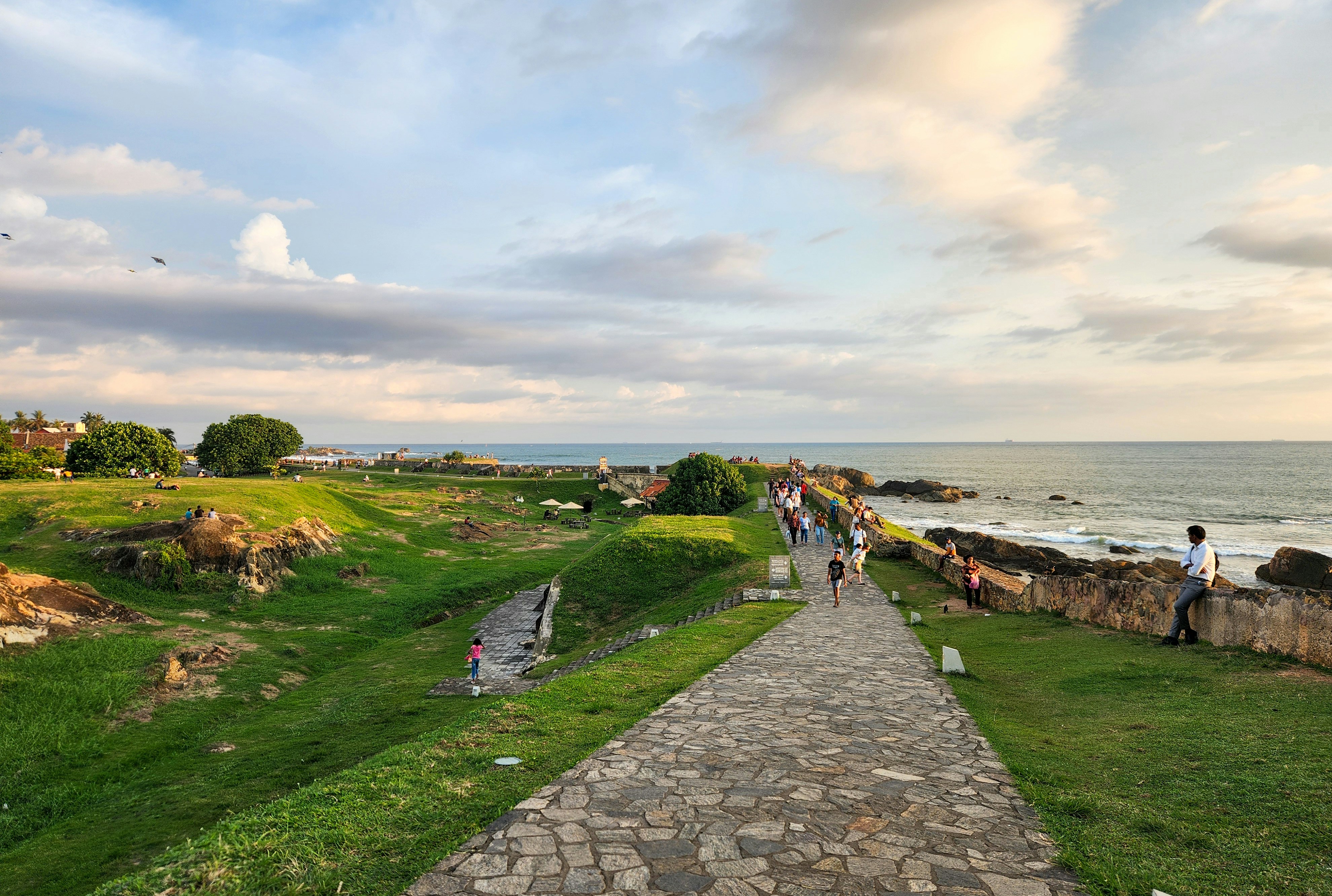 Path leads toward the ocean under a cloudy sky.