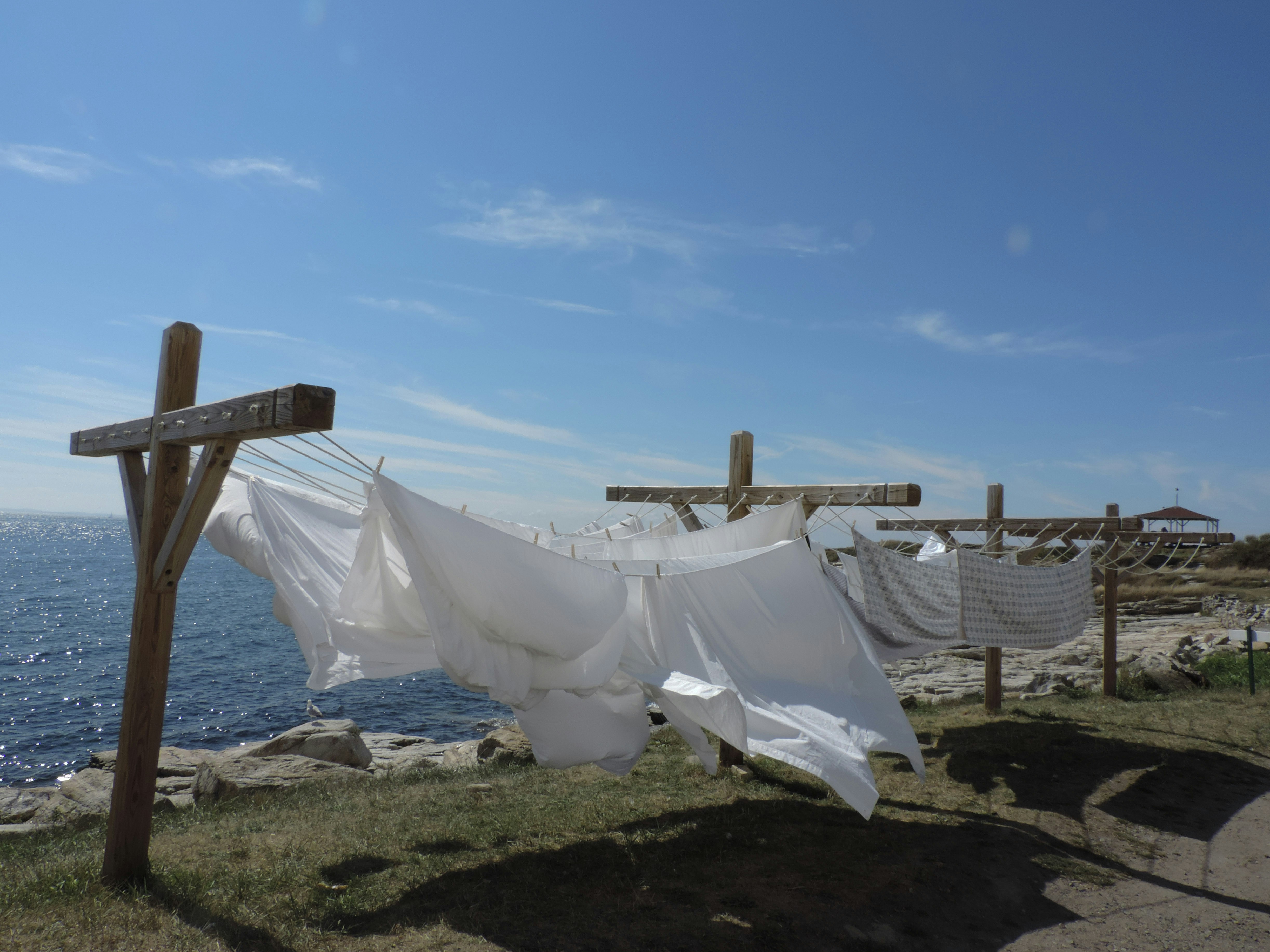 White sheets hang on a clothesline near the ocean.