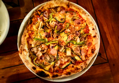 A wood-fired pizza loaded with toppings, presented on a plate