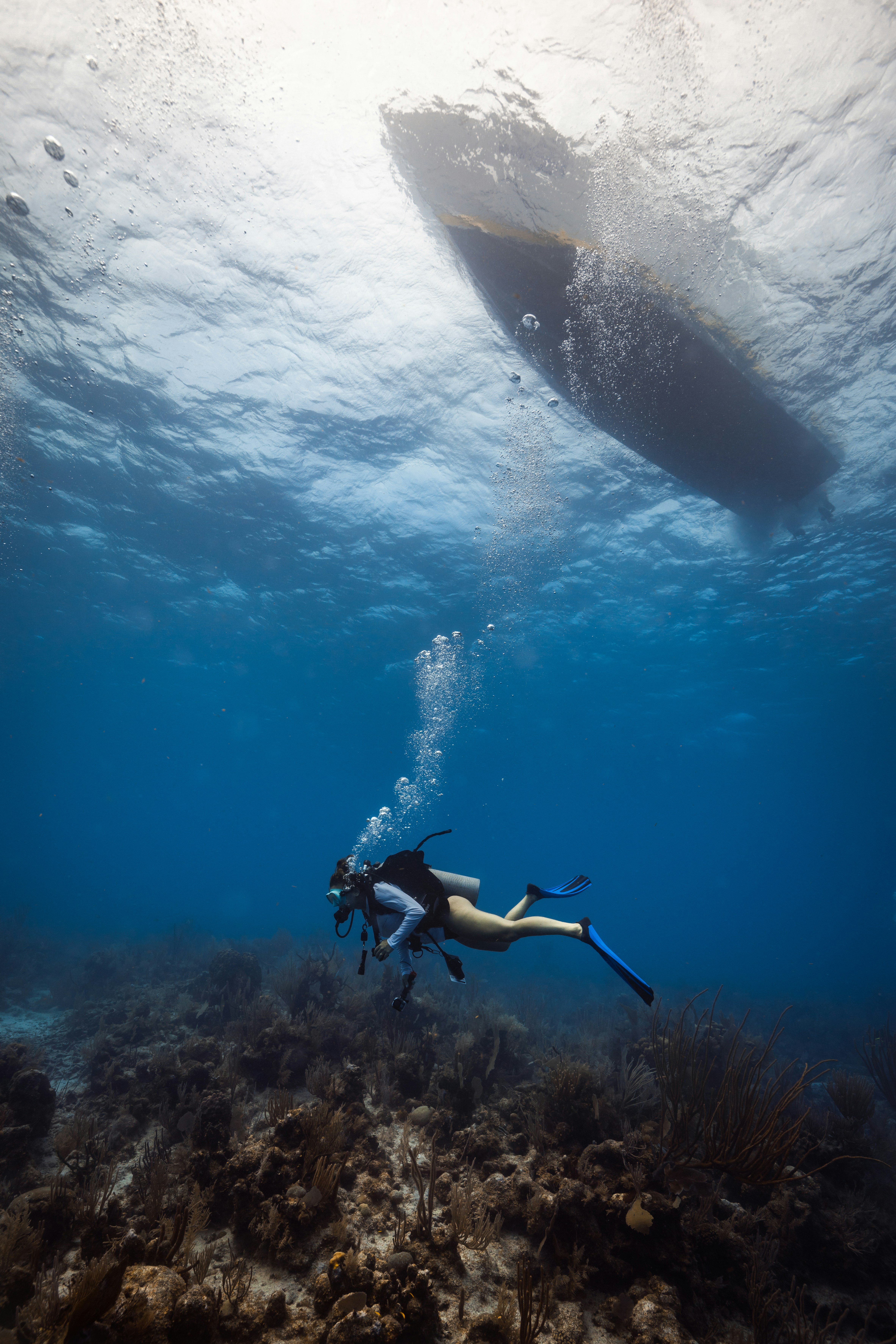 A scuba diver swims near a boat underwater.