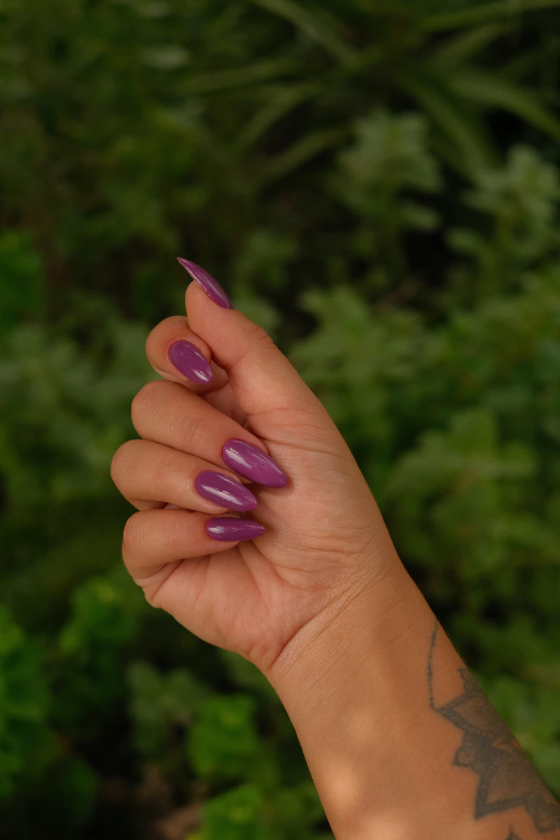 Hand mit glänzenden Nägeln in Mauve-Violett vor Grün