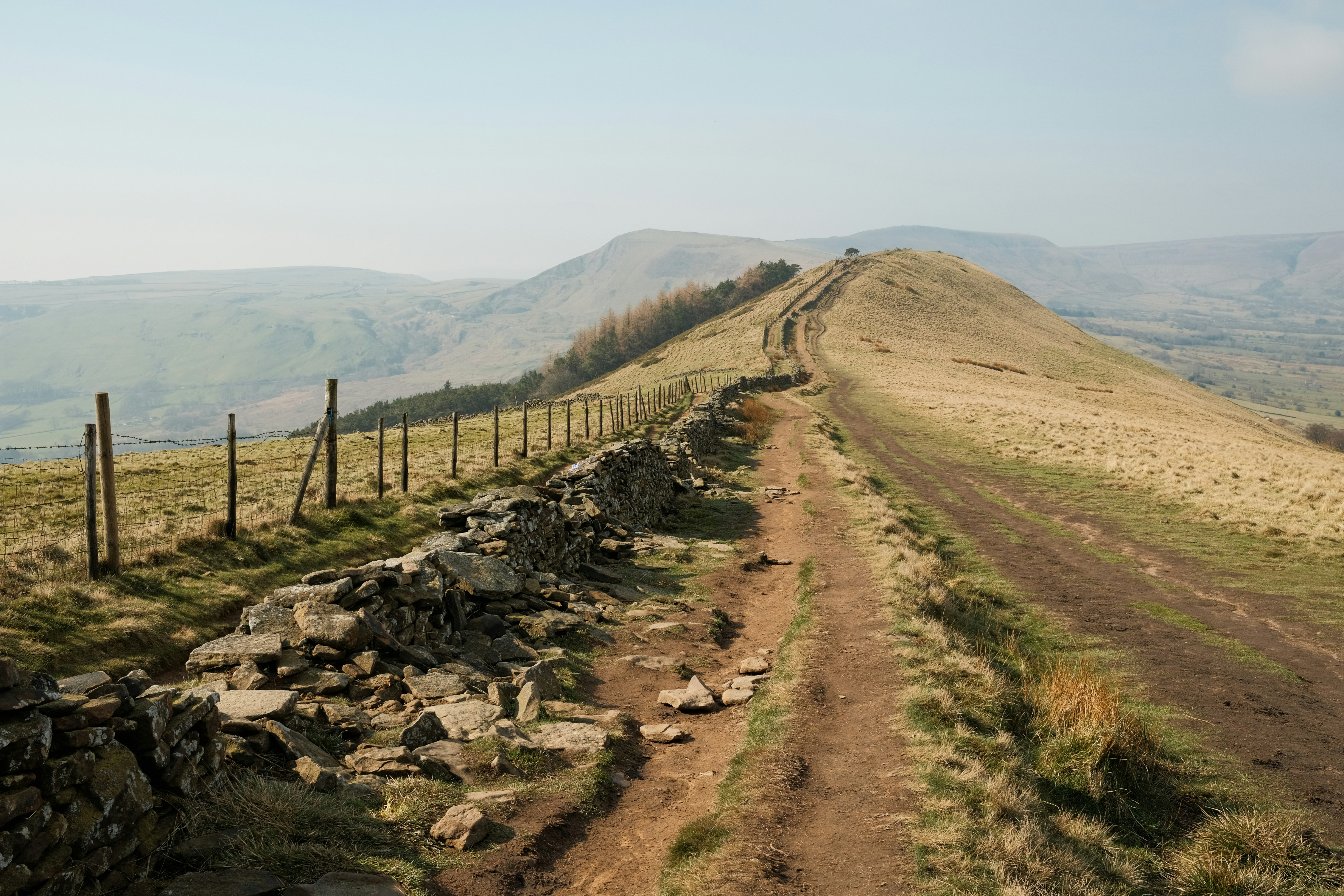 A ridge trail leads to a distant, rolling mountain.