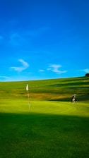 Golf course with flag, bag, and blue sky.