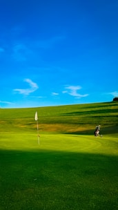 Golf course with flag, bag, and blue sky.