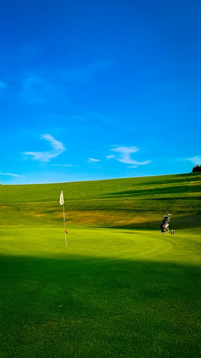 Golf course with flag, bag, and blue sky.