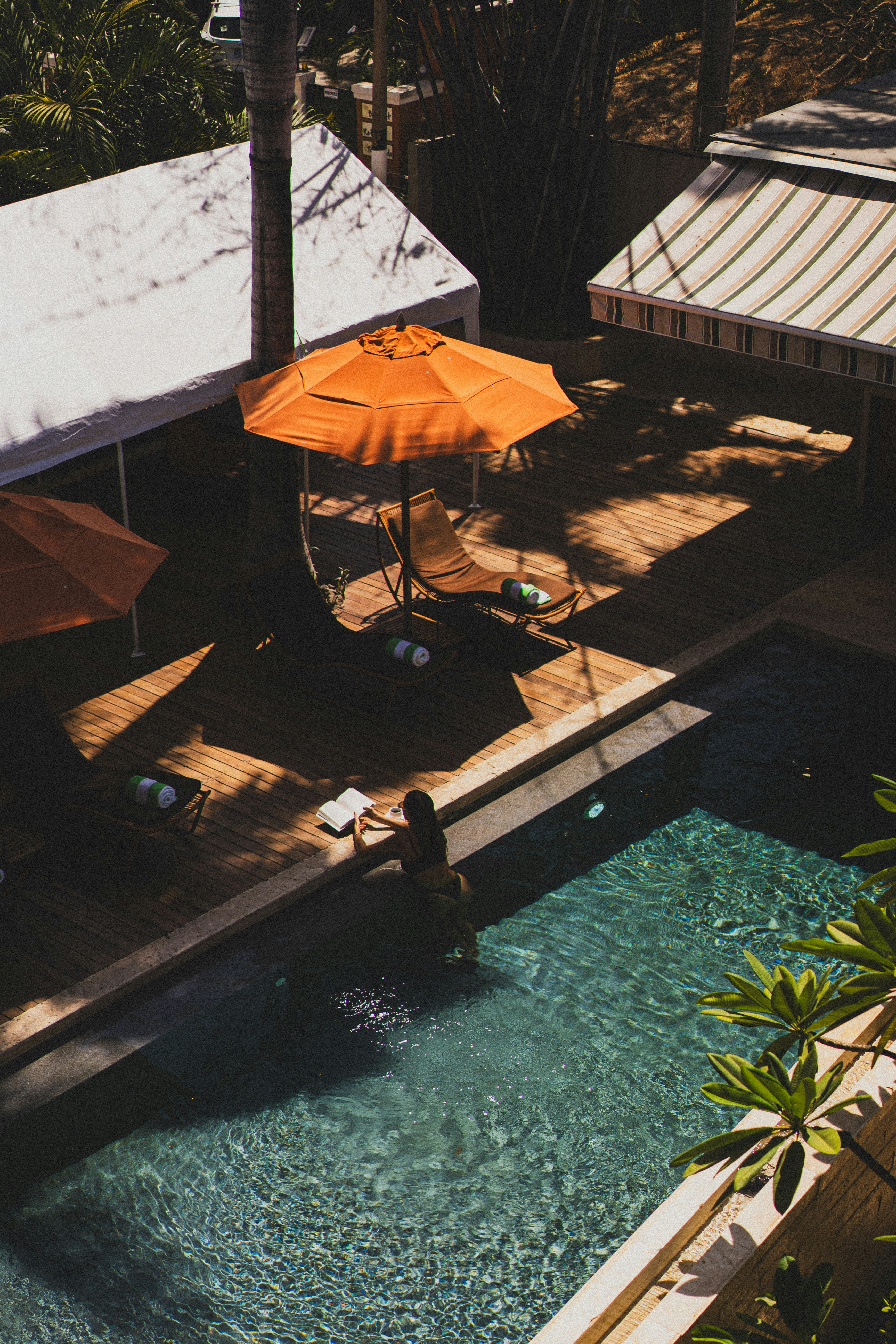 Woman enters the pool near orange umbrellas.