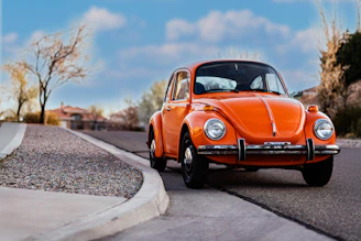 An orange volkswagen beetle is parked on the road.
