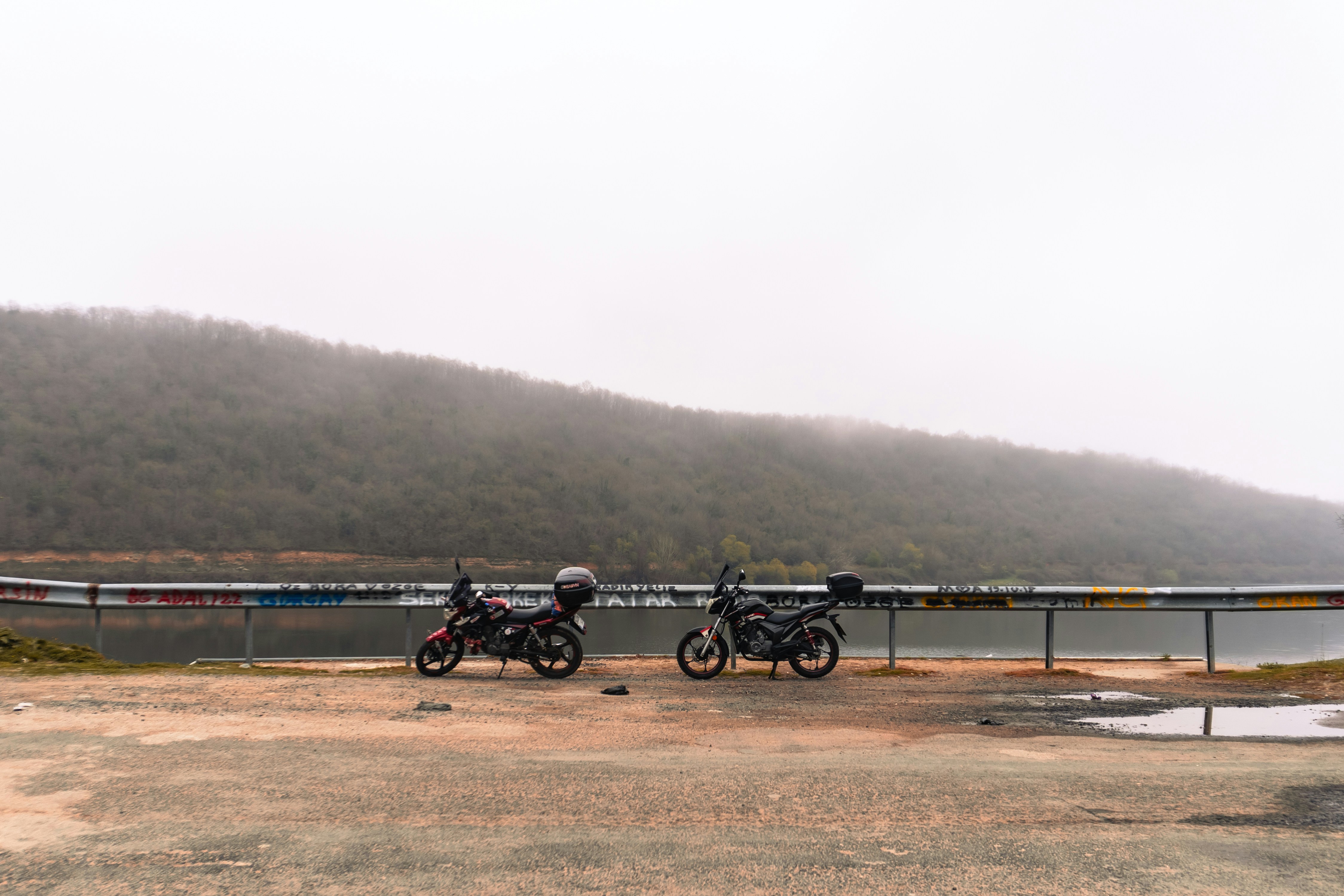 Two motorcycles parked by a lake on a misty day.