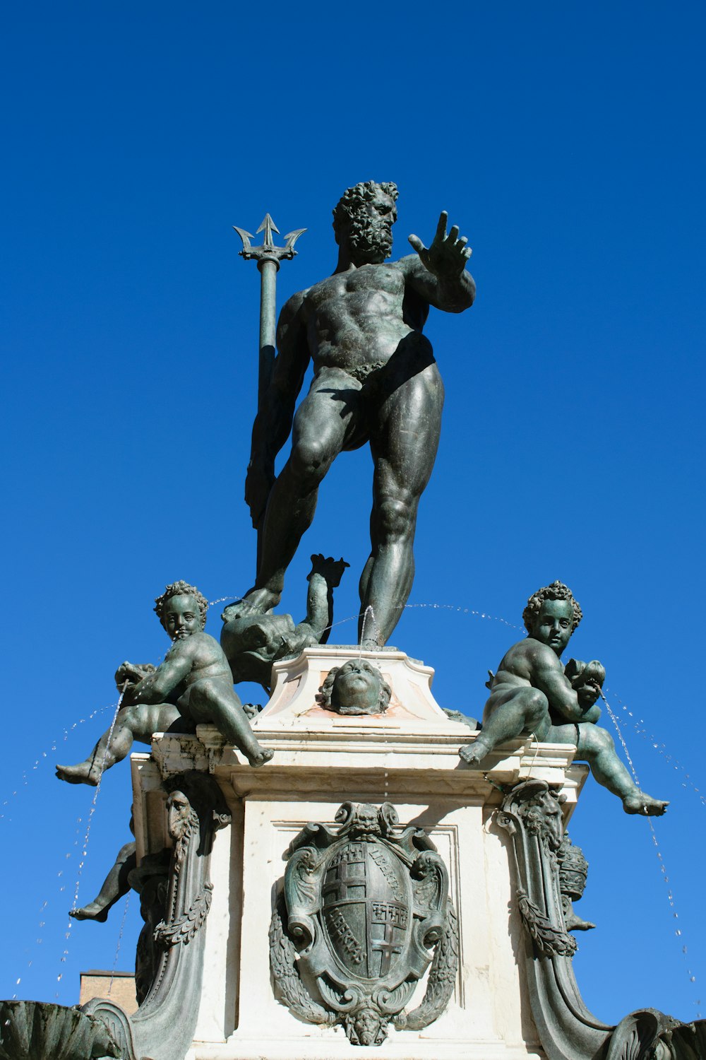 Bronze statue of Neptune holding a trident against a blue sky, the Fountain of Neptune in Bologna
