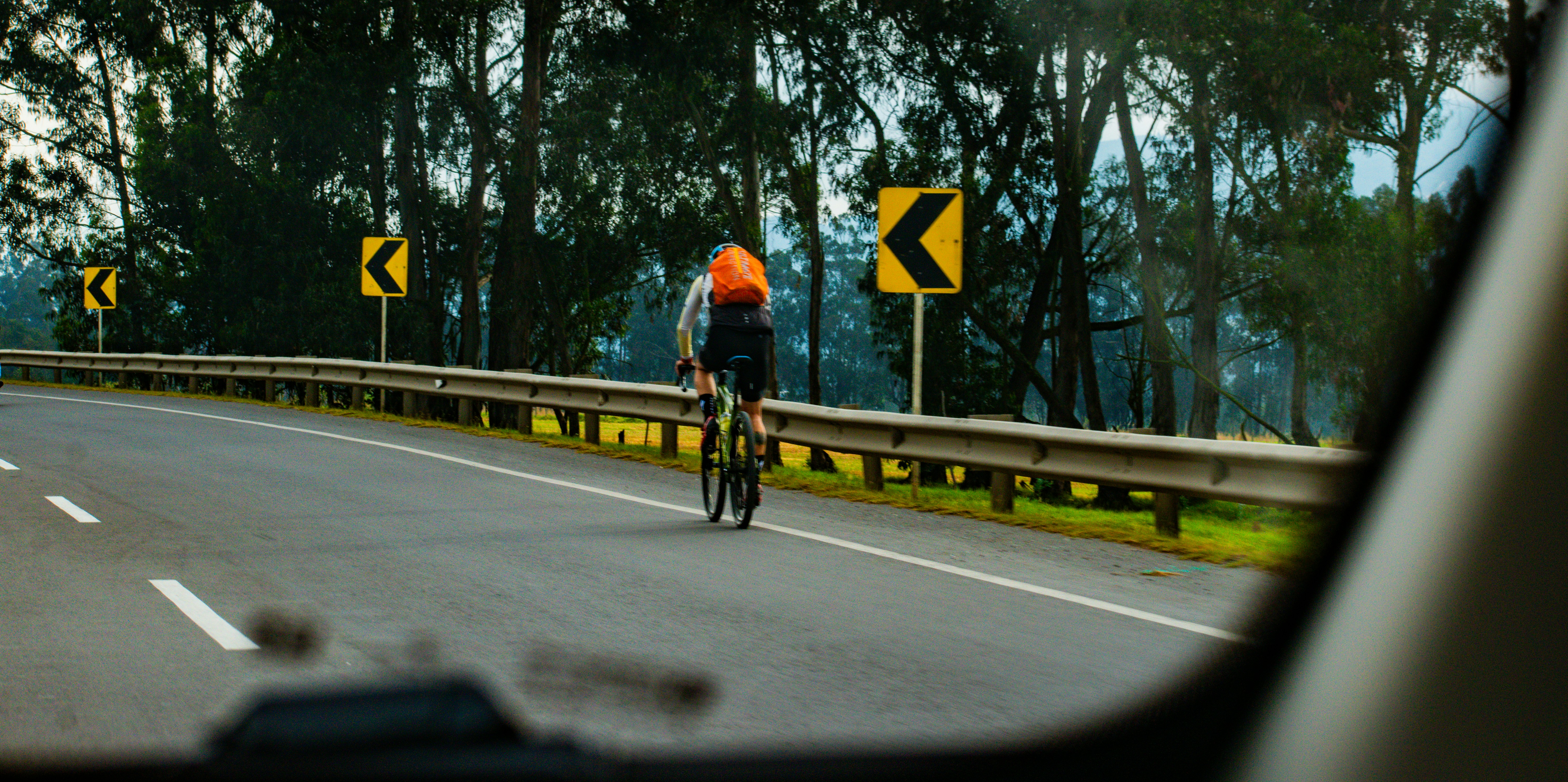 A cyclist rides on a road with warning signs.
