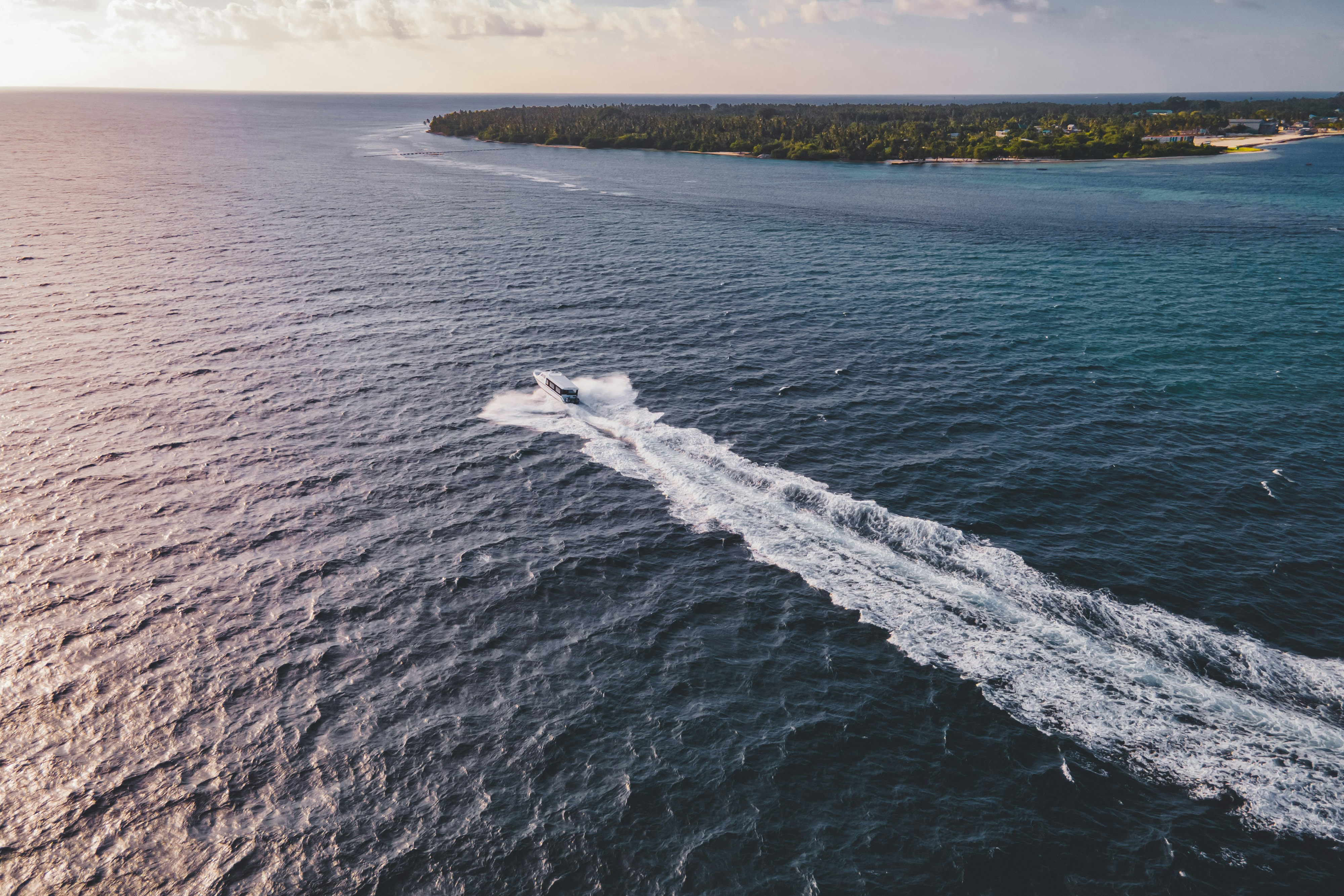 A boat speeds across the ocean towards land.