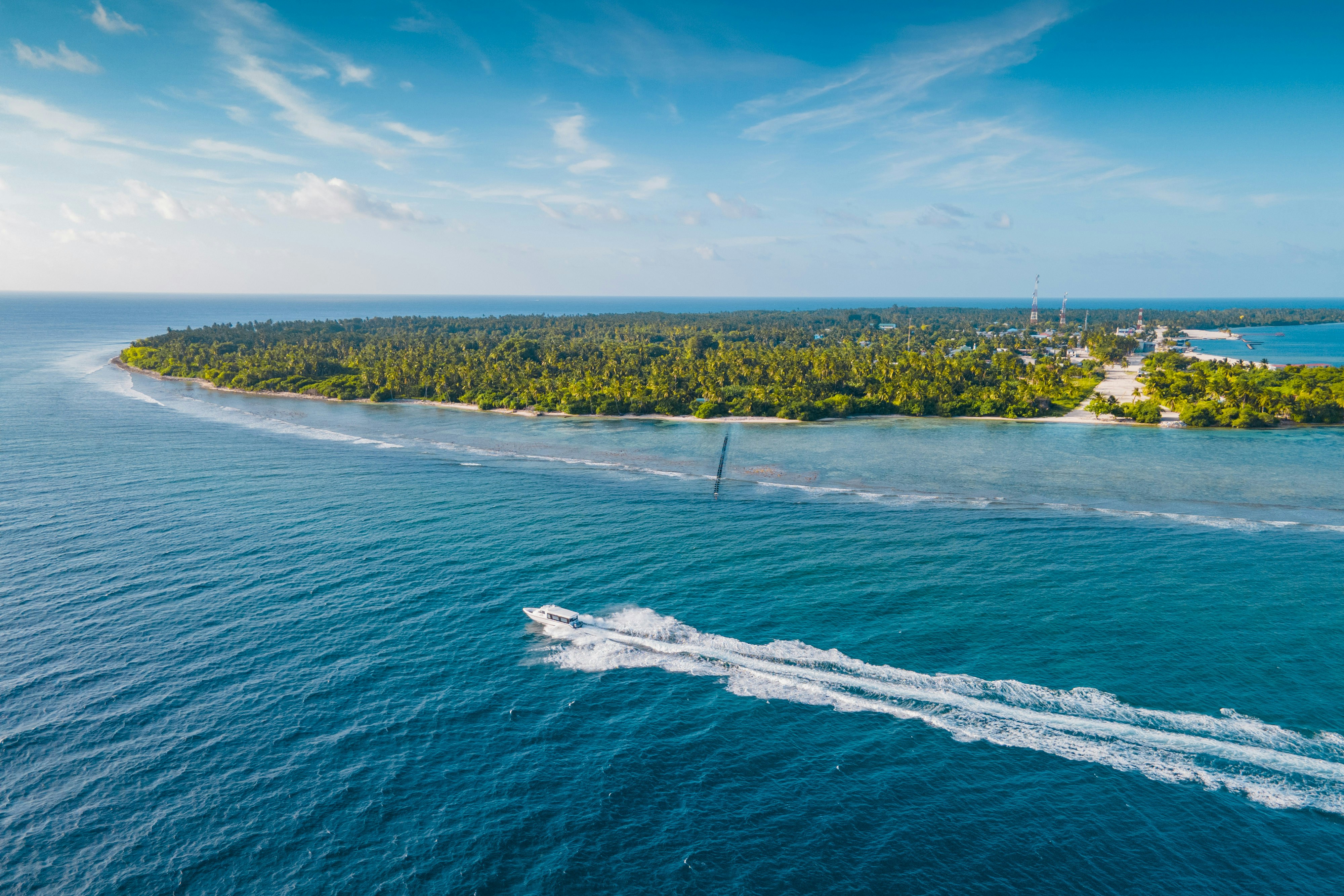 A boat races towards an island in turquoise waters.