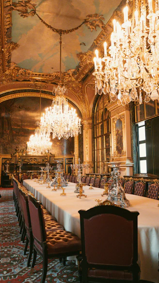 An ornate dining hall with chandeliers and a long table.