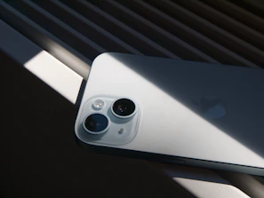 An iPhone rests under sunlight, its camera visible.
