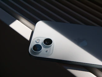 An iPhone rests under sunlight, its camera visible.
