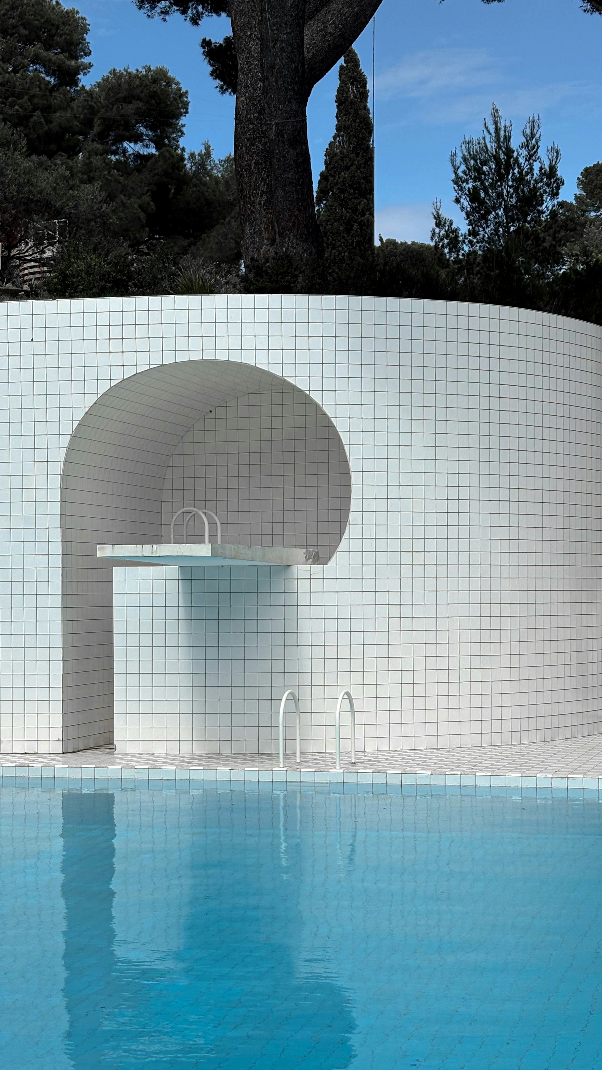 Pool with diving board next to tiled wall.