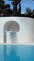 Pool with diving board next to tiled wall.