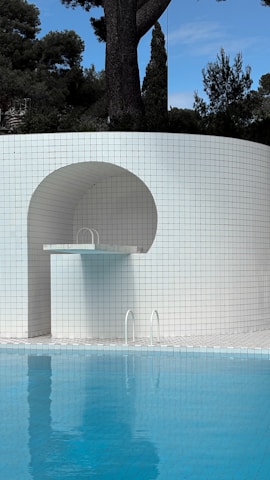 Pool with diving board next to tiled wall.