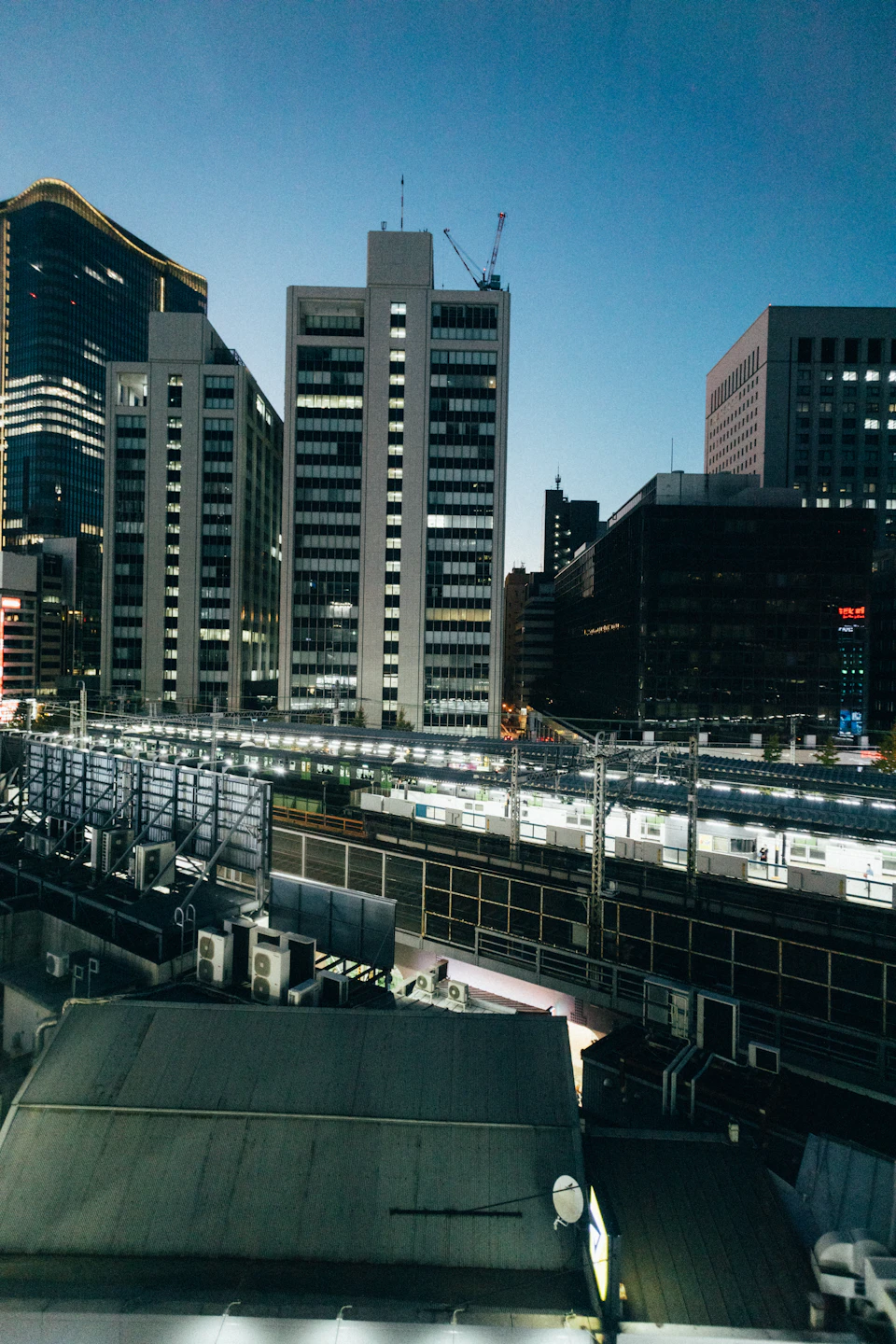 Tall city building with multiple windows reflecting surrounding lights at night