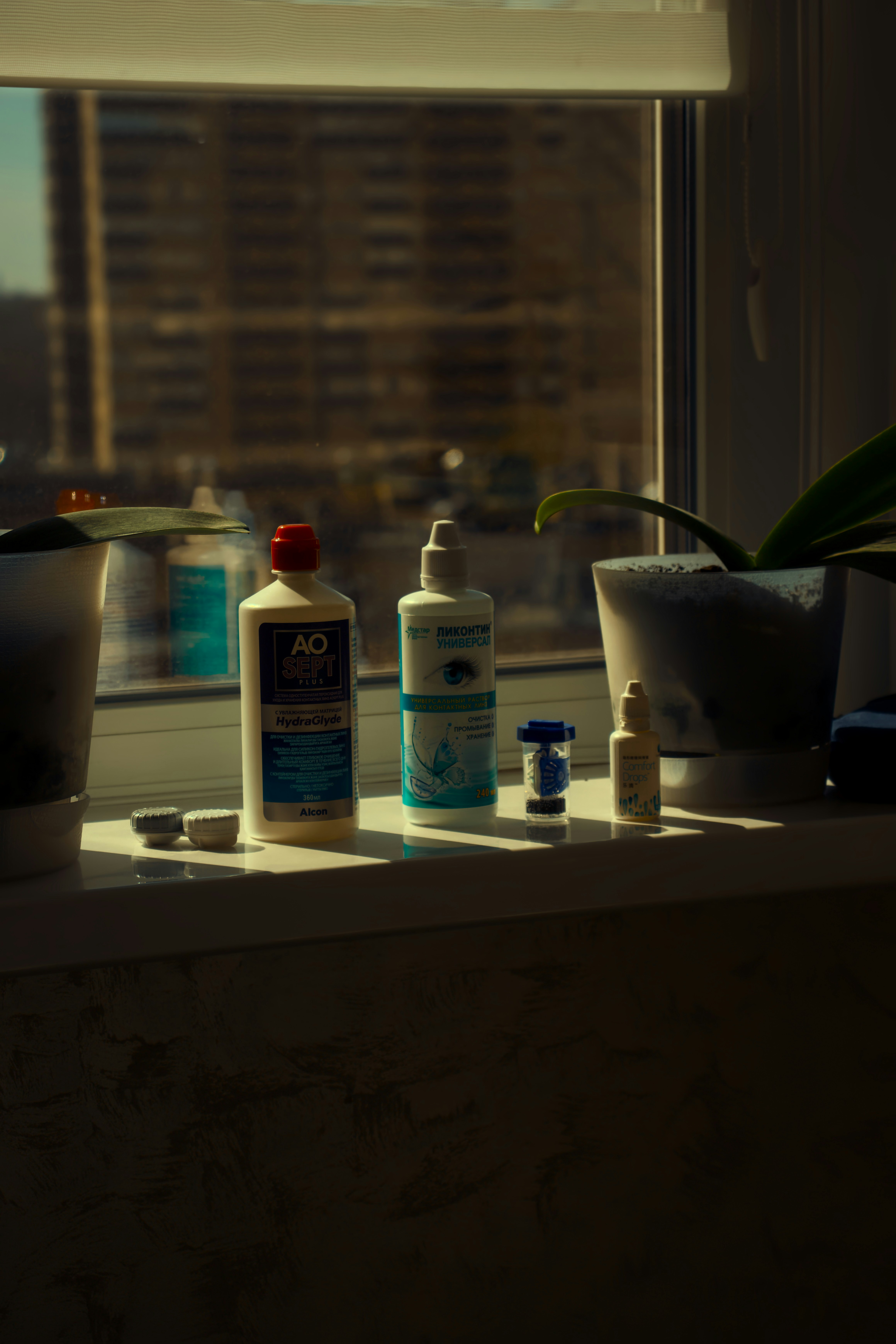 Contact lens solutions sit on a sunlit windowsill.