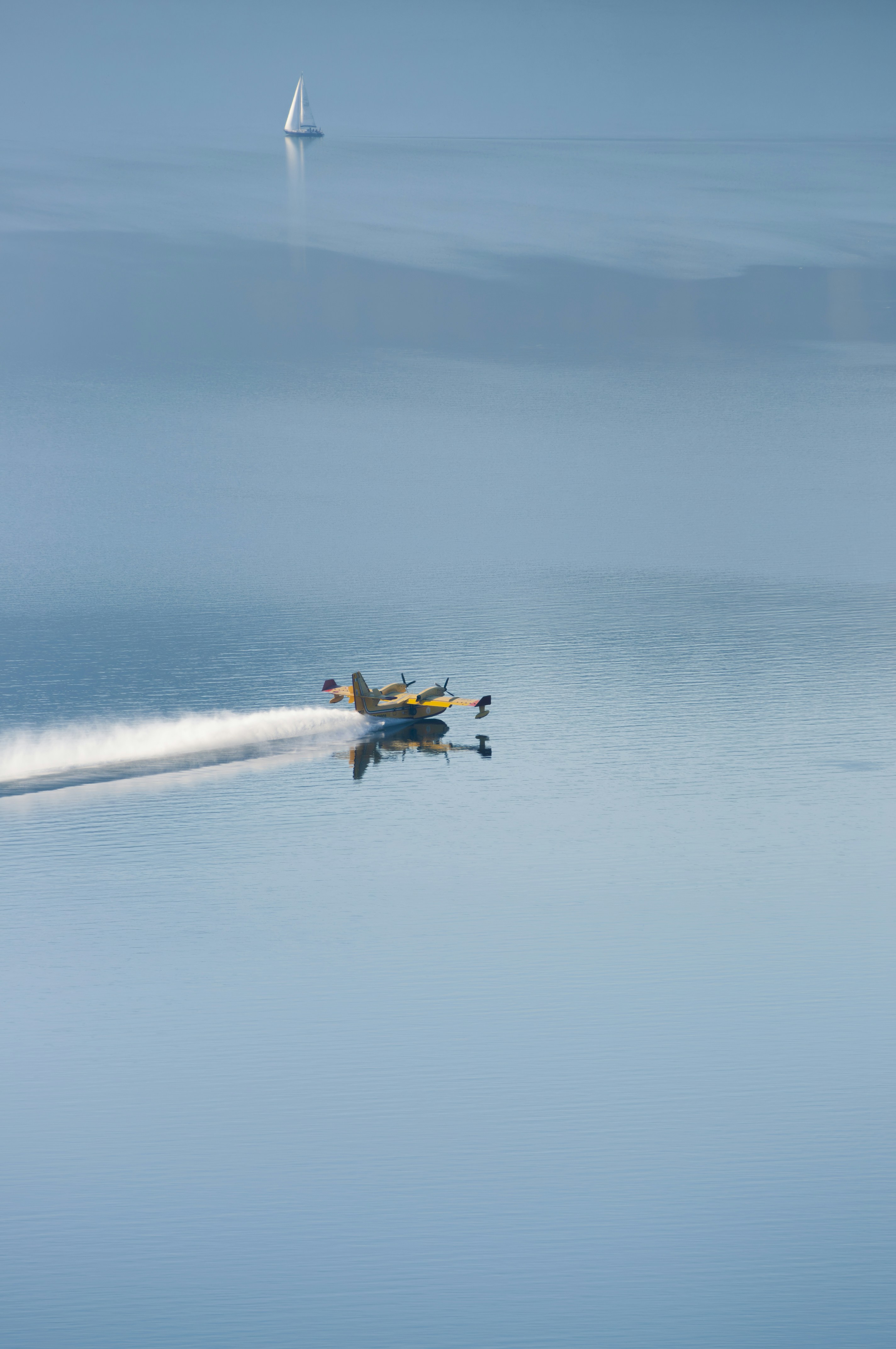 A seaplane skimming the water with a sailboat