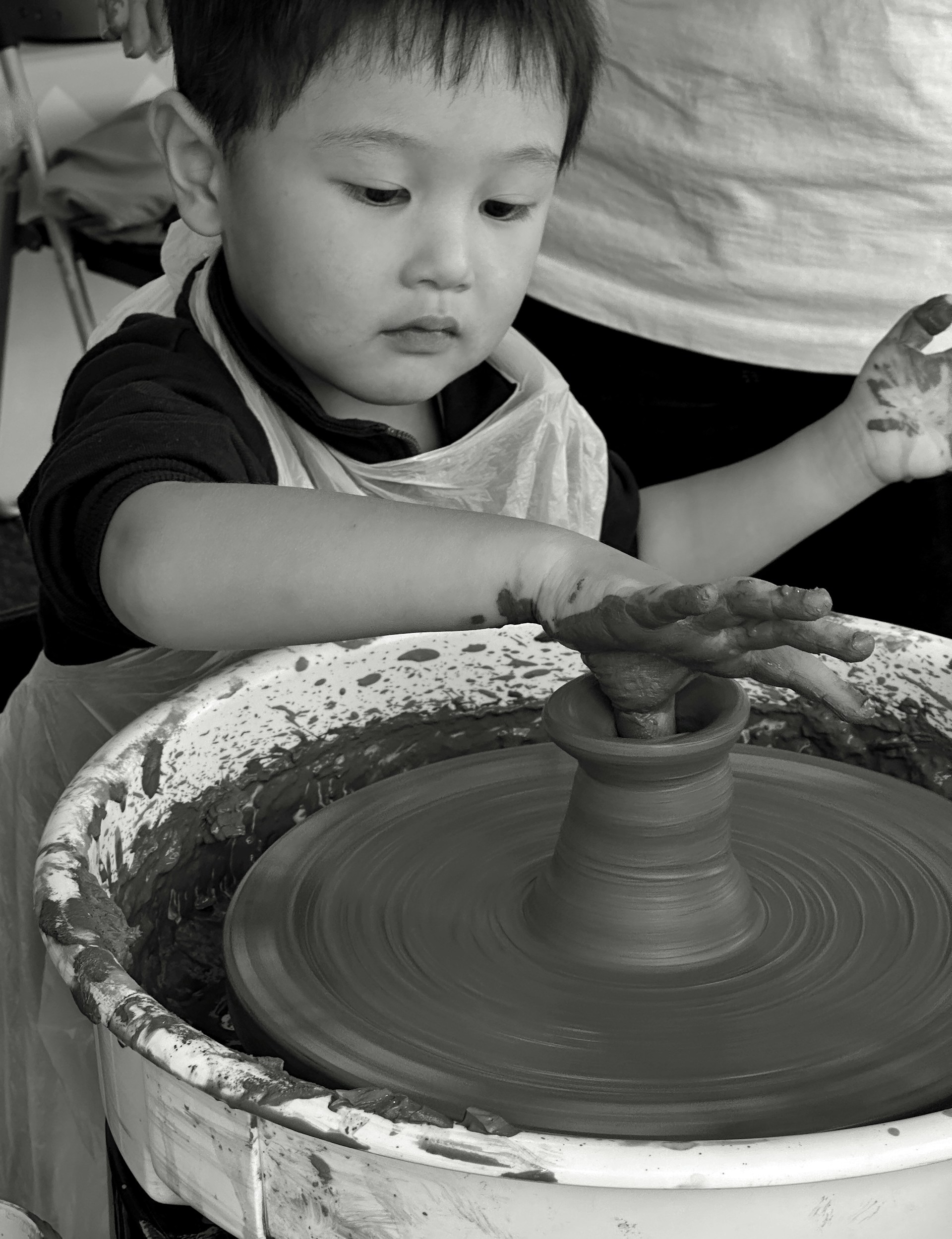 A little boy creates pottery on a wheel.