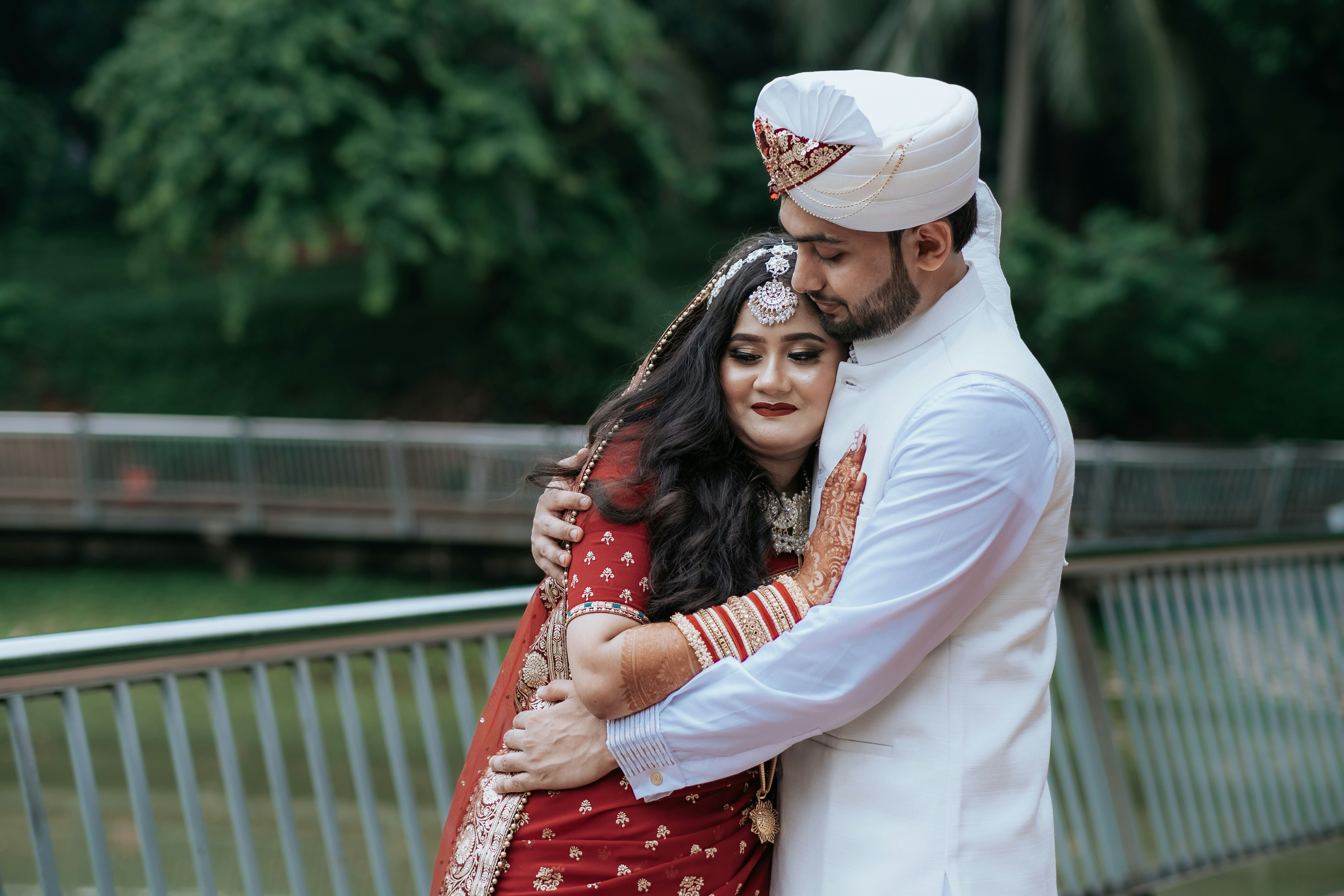 A newlywed couple embraces affectionately in a park.