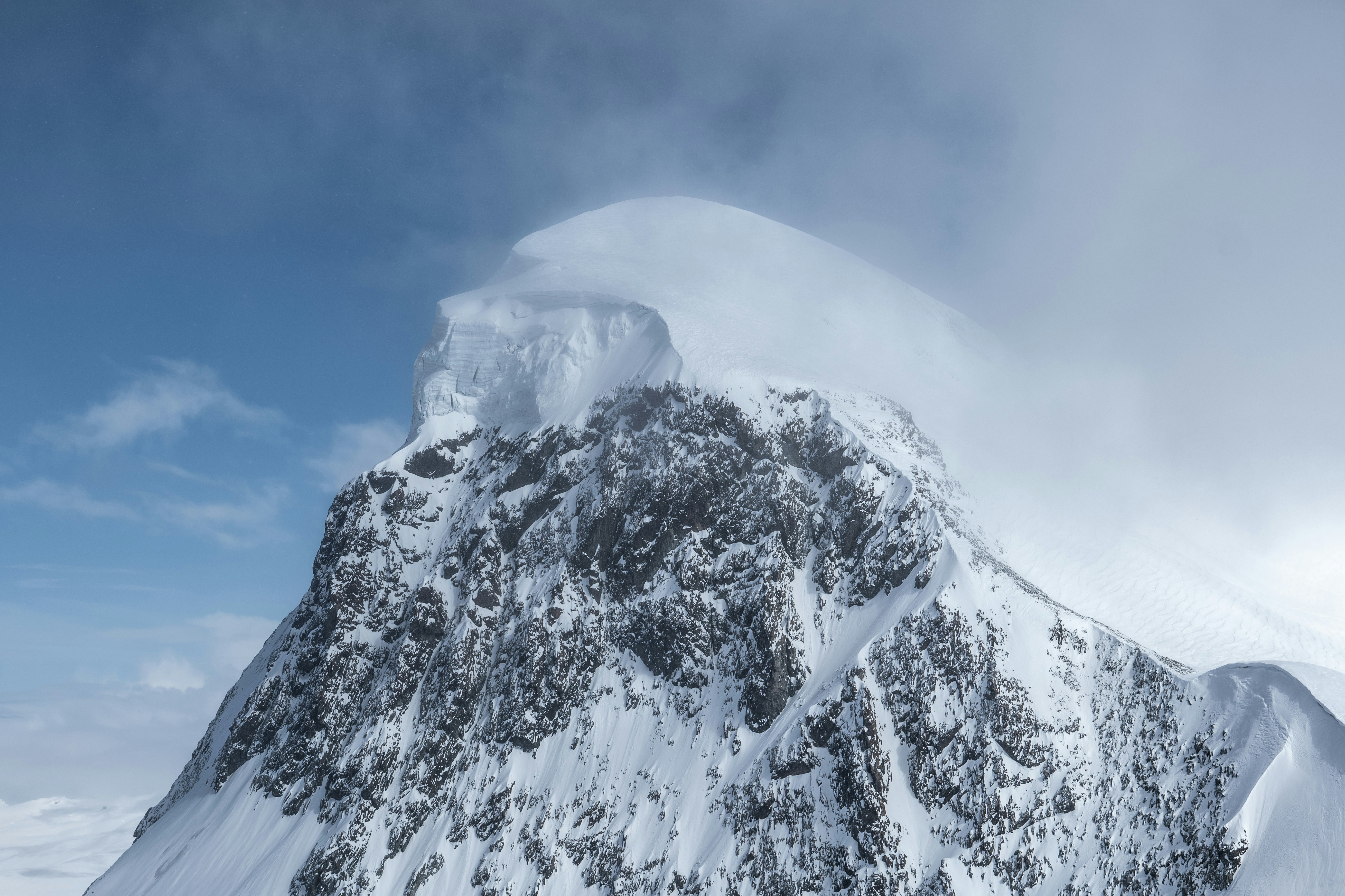 Snow-capped mountain with windswept clouds above.