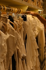 Clothes on a rack are being browsed by a hand.