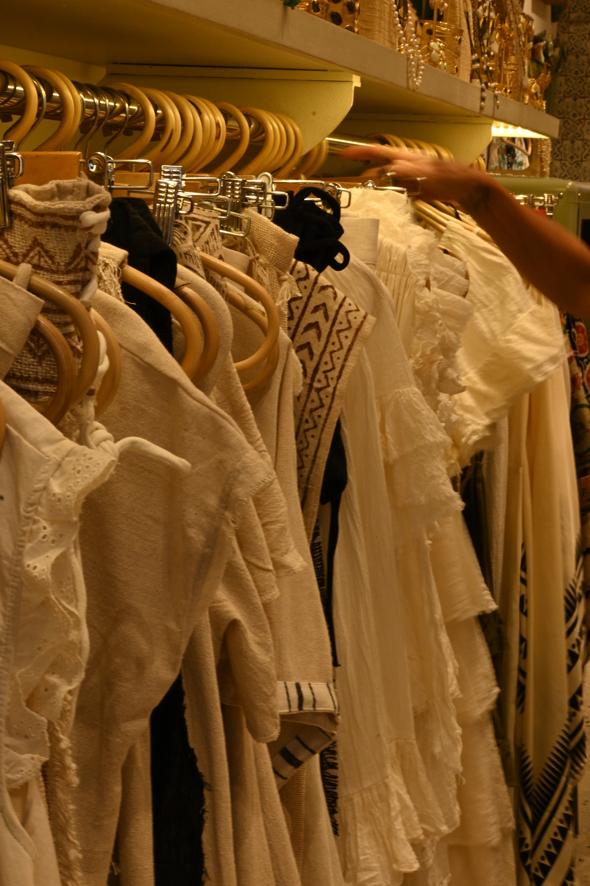 Clothes on a rack are being browsed by a hand.