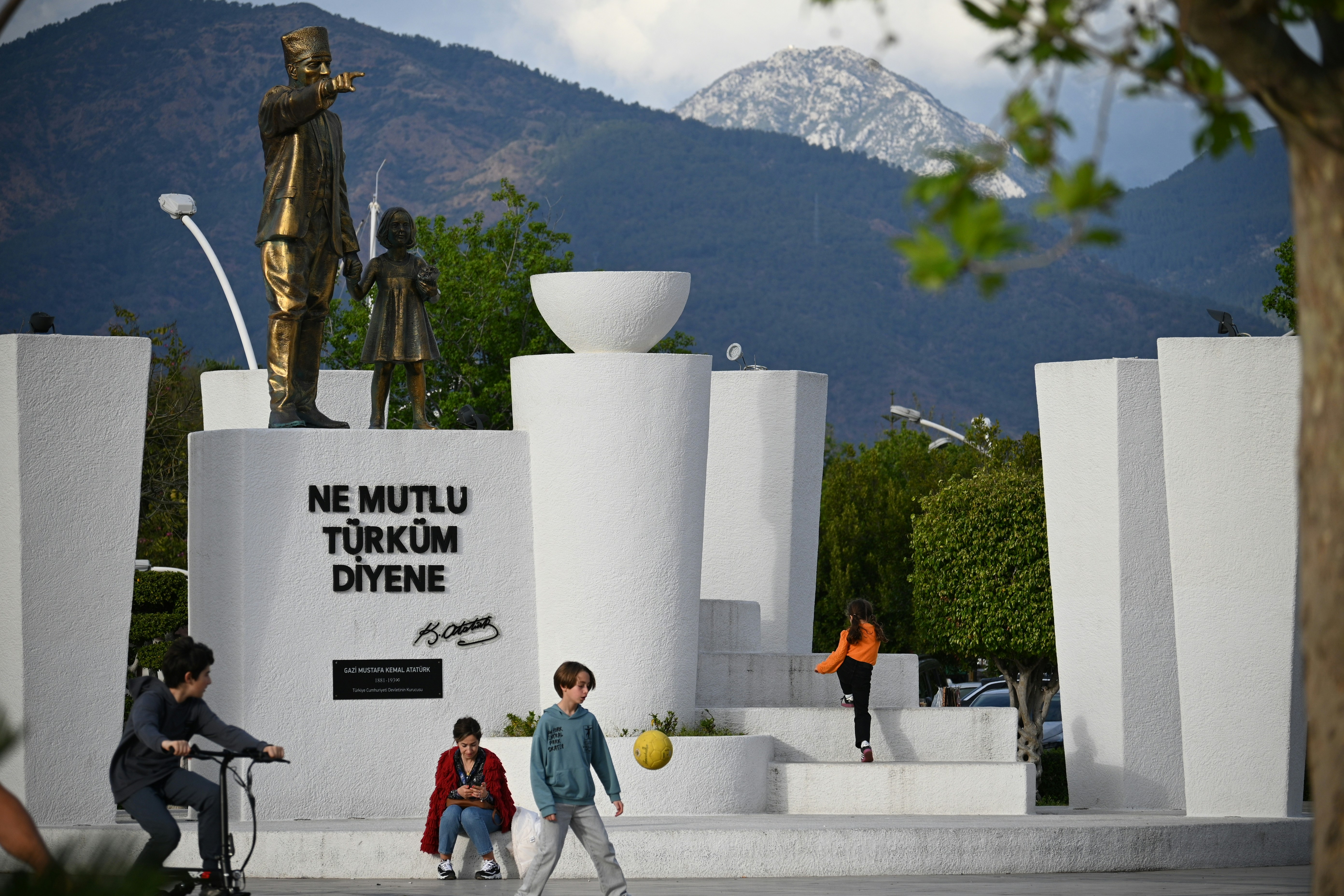 People play near a monument with mountains in the background.