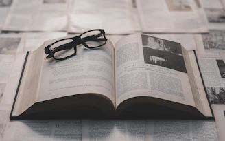 Glasses rest on an open book surrounded by papers.