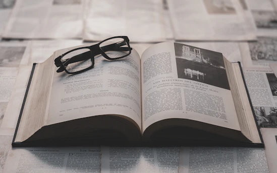 Glasses rest on an open book surrounded by papers.