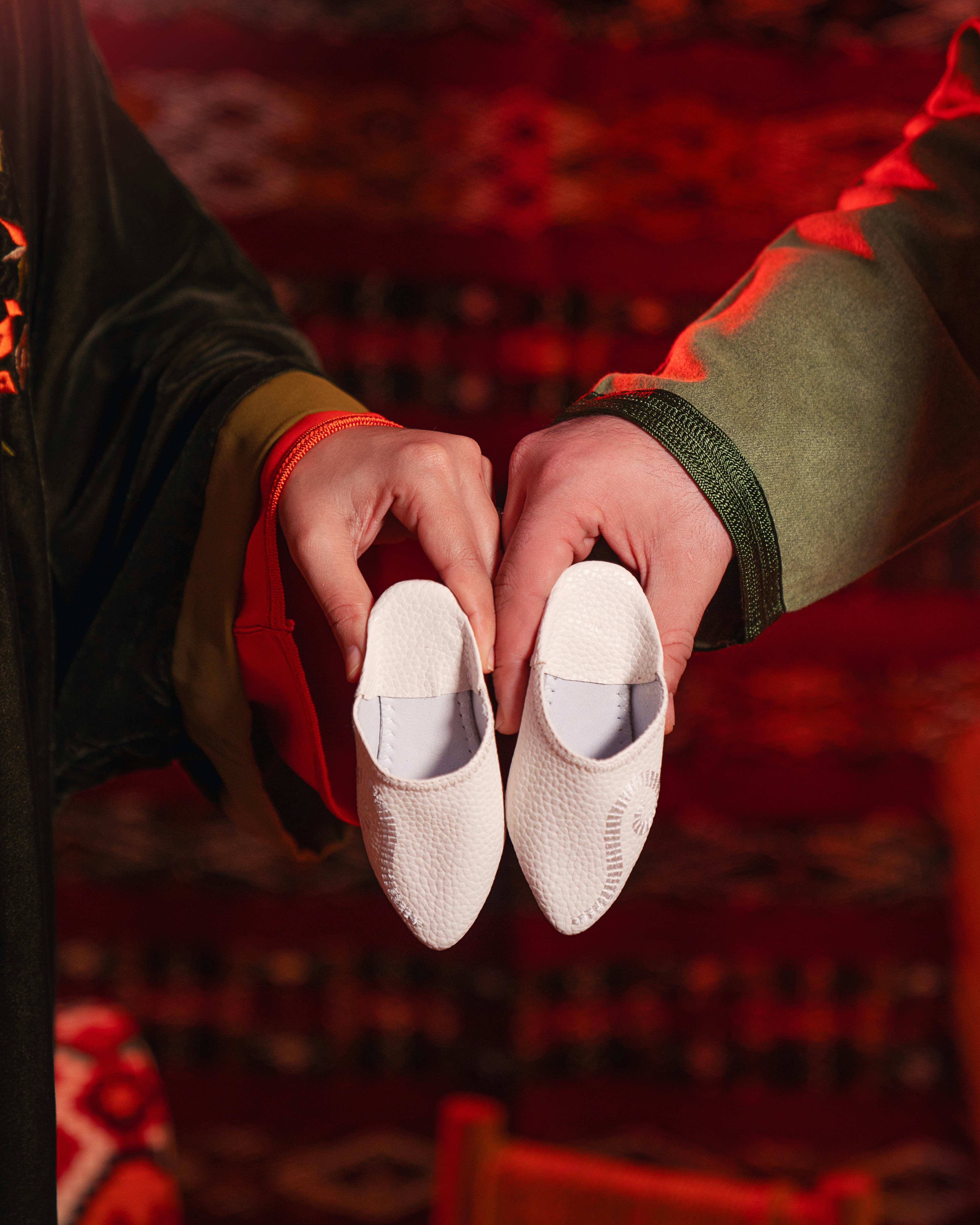 Hands hold tiny white baby shoes.