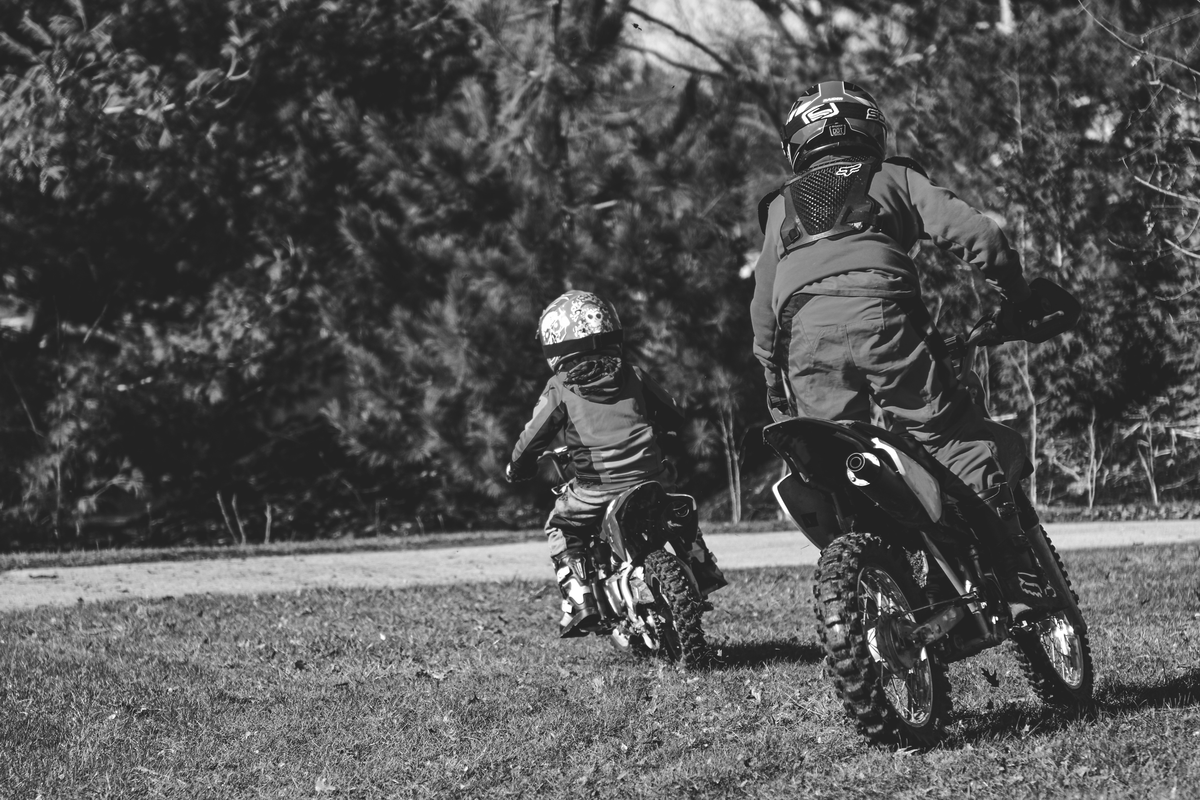 Two children ride dirt bikes on a grassy field.