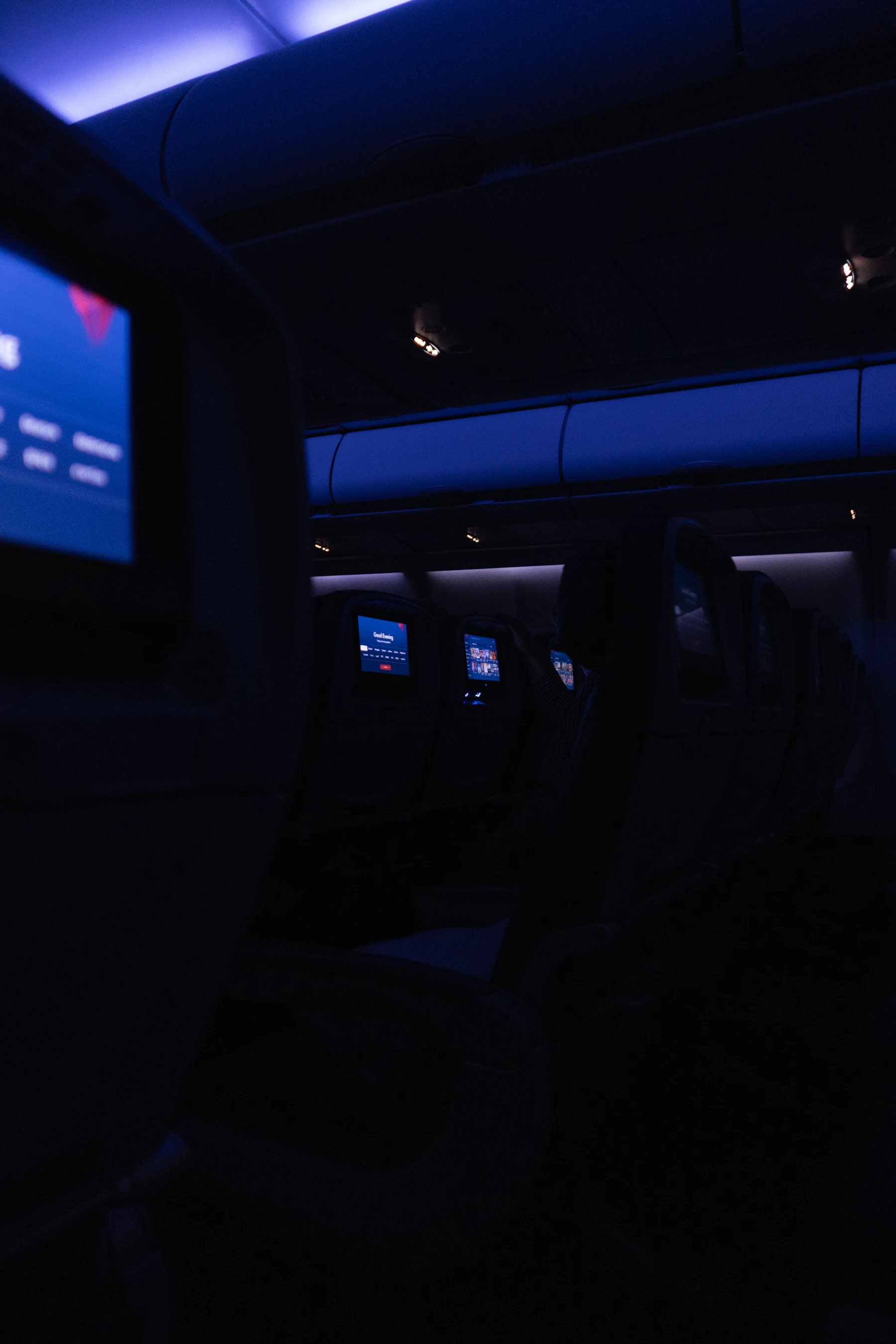 A dark aircraft cabin lit by blue overhead lights during an overnight flight.