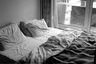 A bed is unmade near a window.