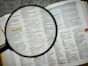 Magnifying glass focuses on a dictionary page.