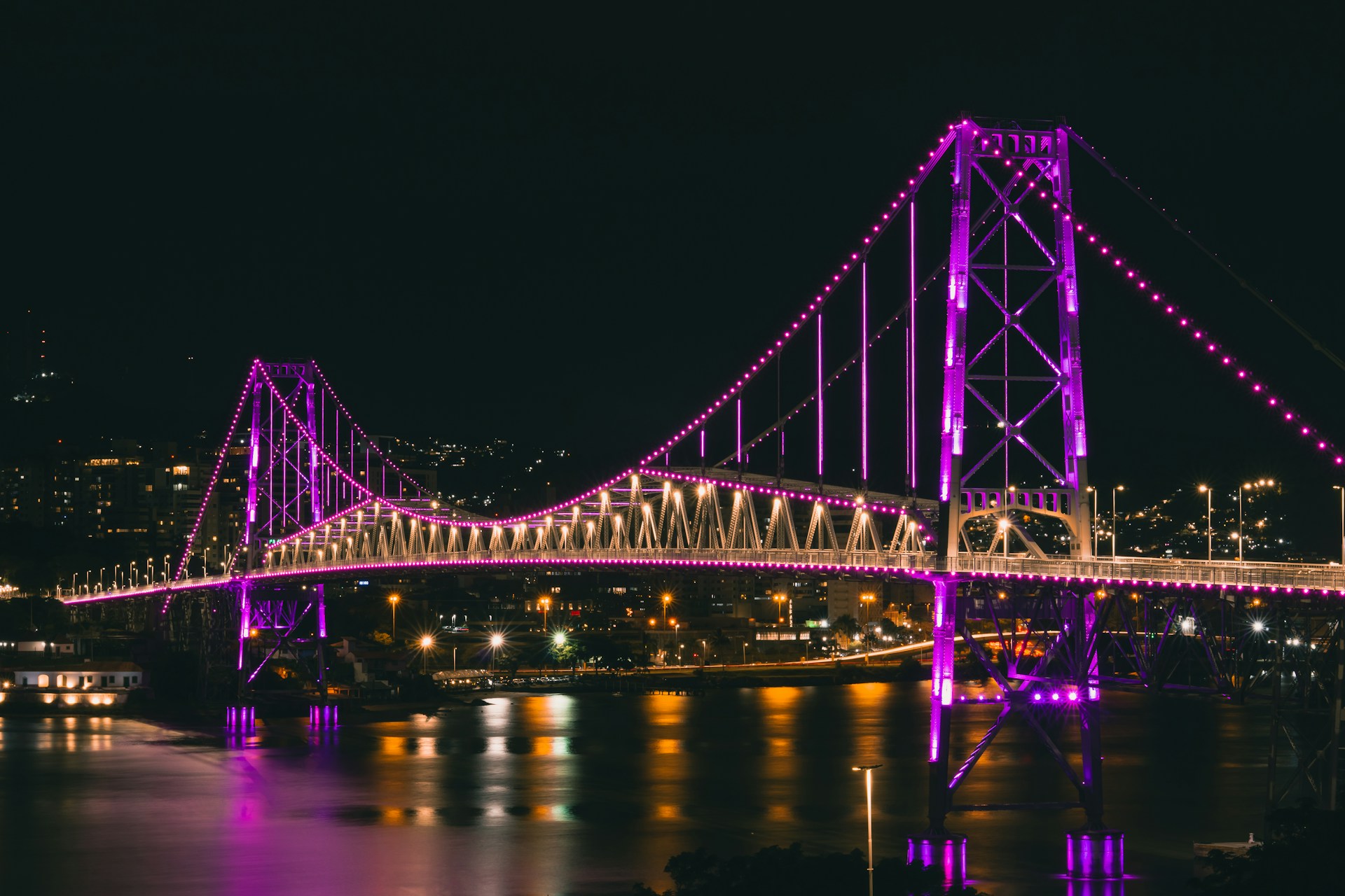 A beautiful bridge shimmers with purple lights at night.