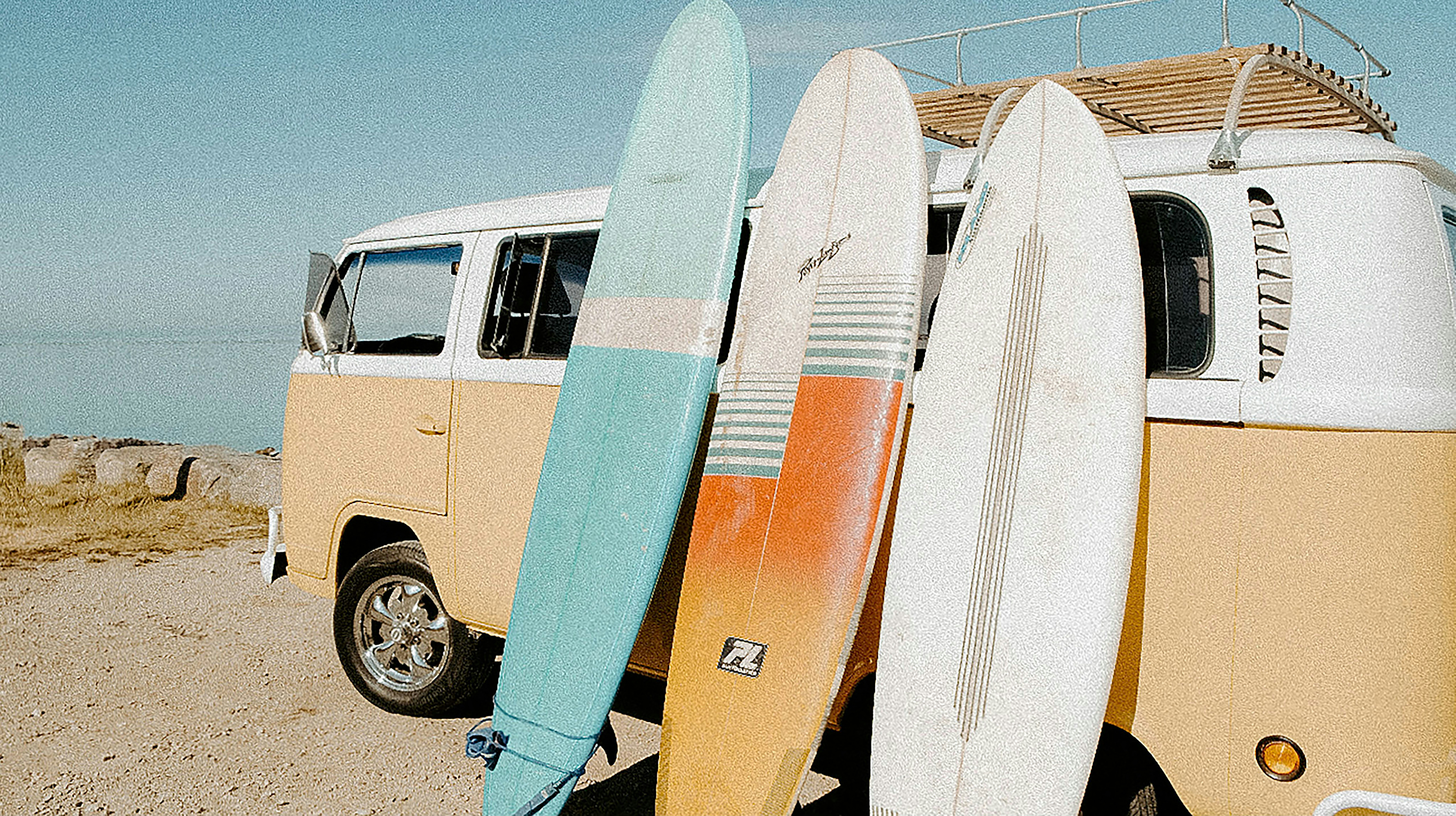 Surfboards lean against a retro van by the sea.