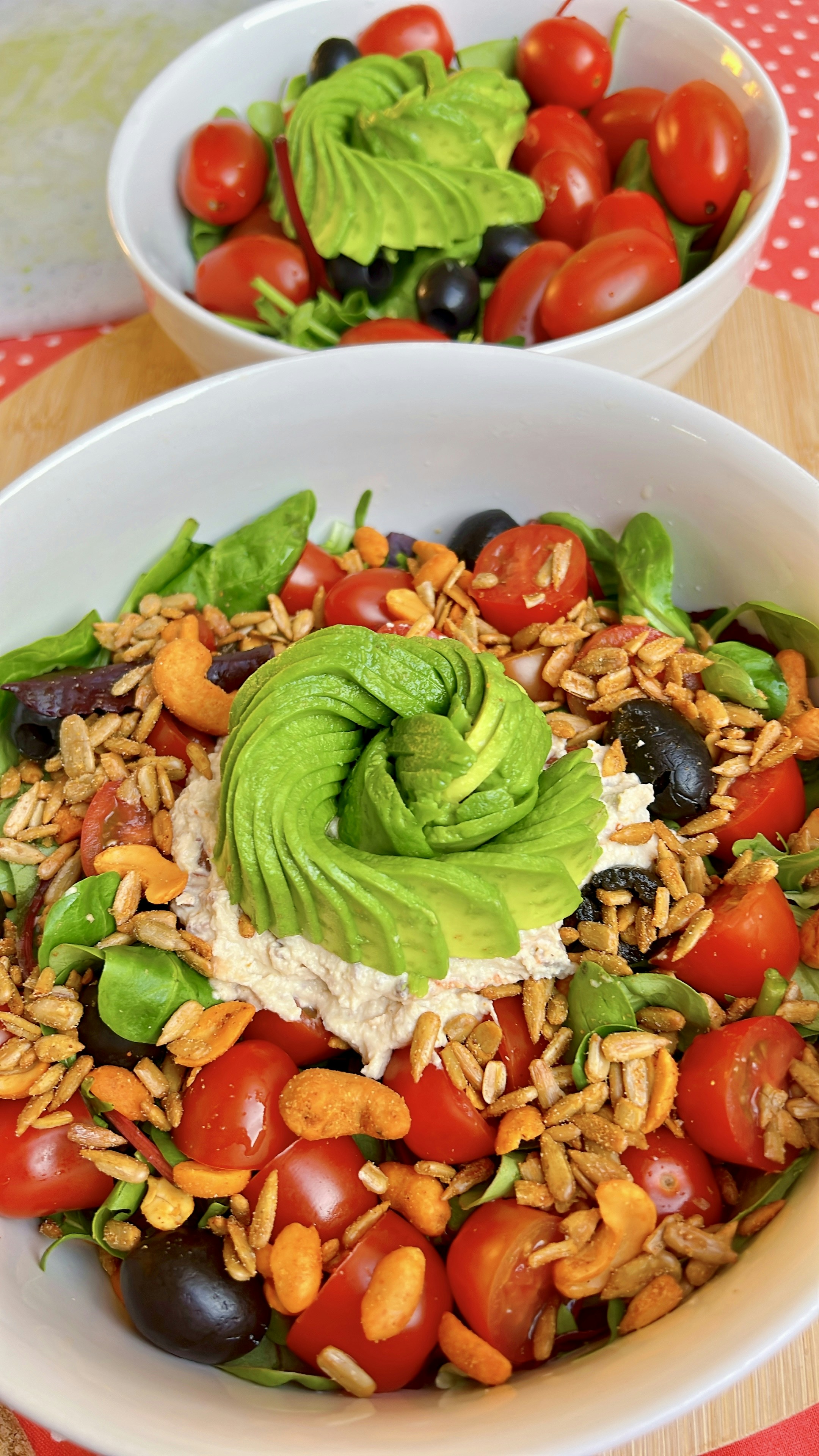 Salads with tomatoes, avocado, and seeds in white bowls.